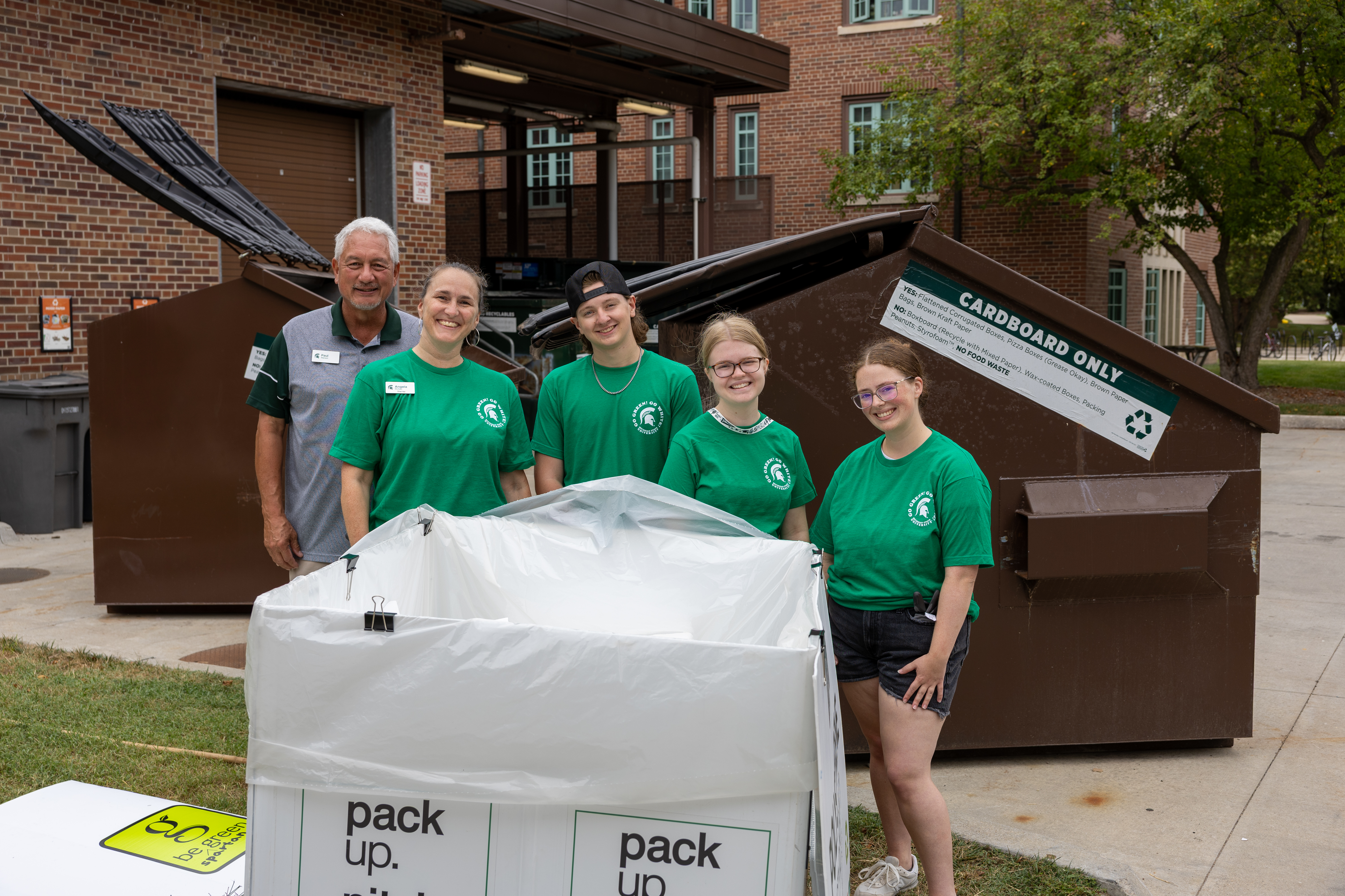 Michigan State University team members wearing green Live On T-shirts stand by recycling bins during move-in, helping with cardboard collection and promoting campus sustainability.