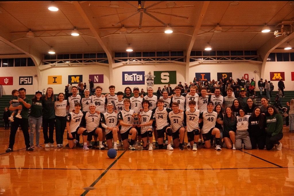 MSU Club Dodgeball team members pose on a gymnasium floor with Big Ten flags displayed in the background.