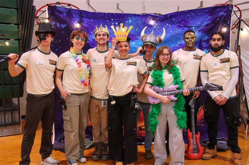 A group of students wearing silly hats pose in front of a backdrop depicting a starry night sky