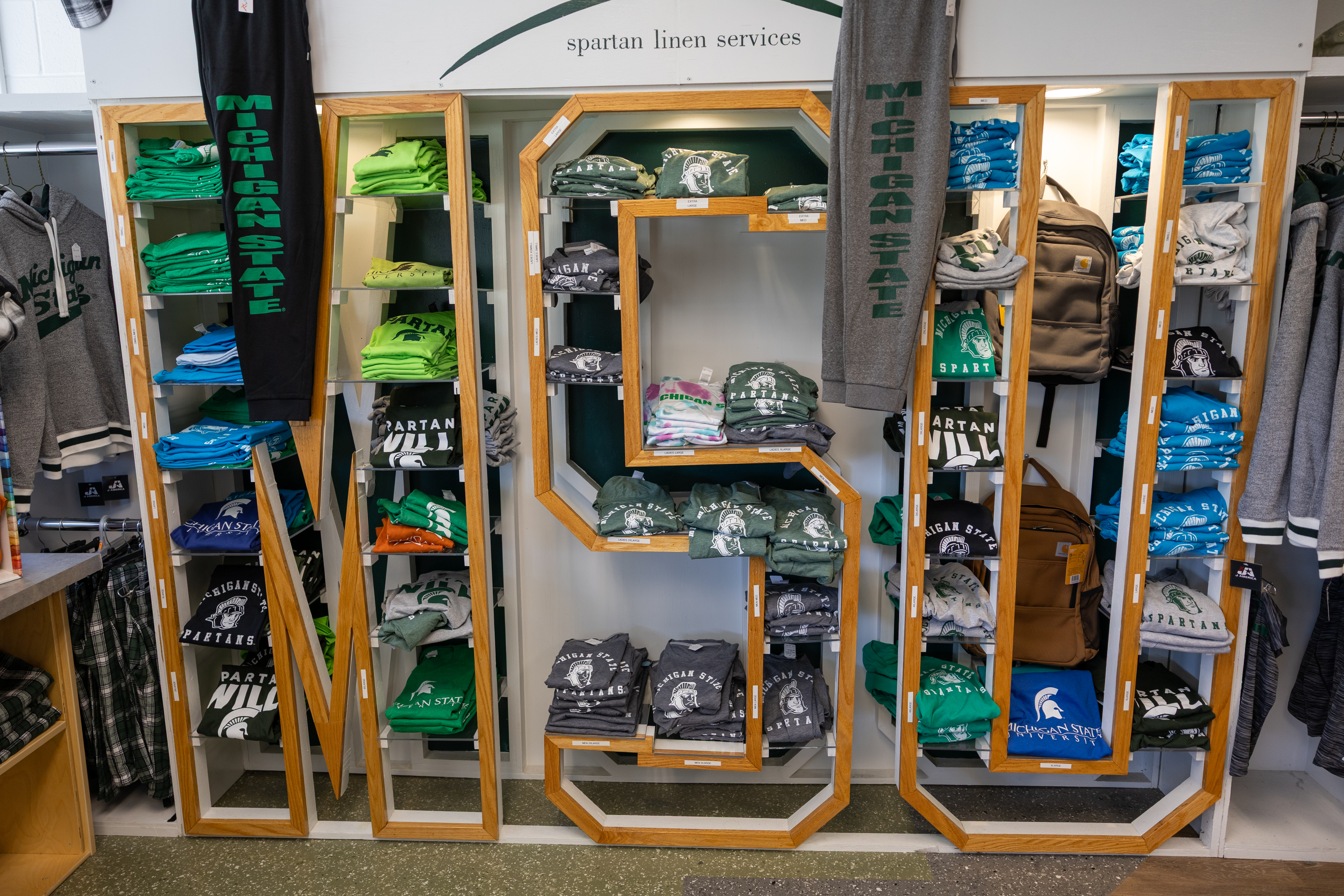 A display at Spartan Linen Services shows available clothing items stacked on shelving in the shape of the letters “MSU."