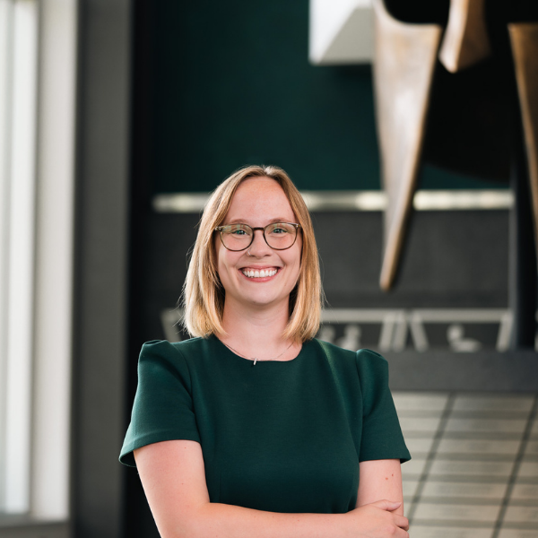 Professional headshot of a Michigan State University staff member in a green dress, standing in front of a Spartan helmet sculpture.