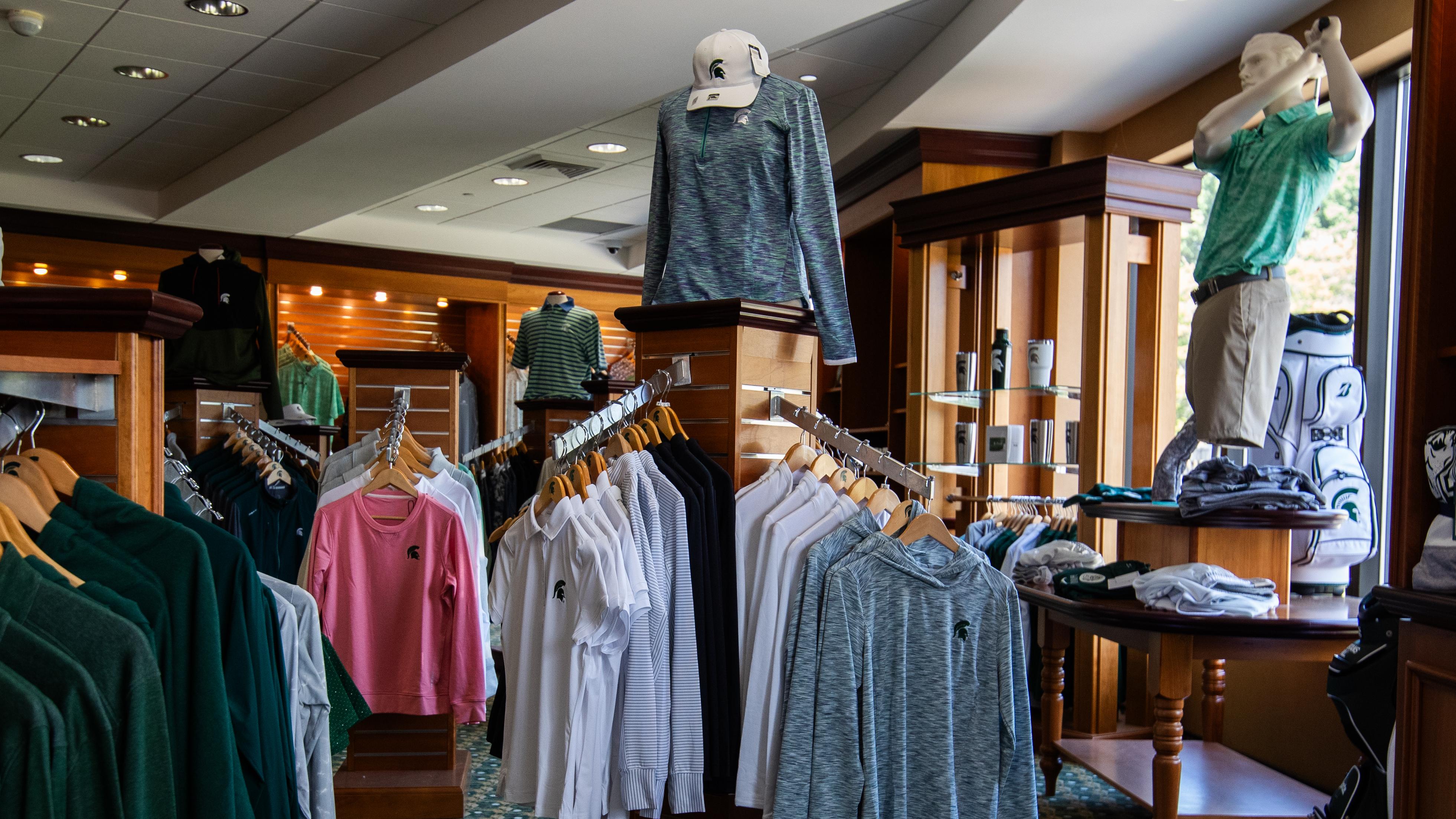Campus store interior with racks of Michigan State University apparel, including green and white shirts, hoodies and hats, plus mannequins displaying outfits